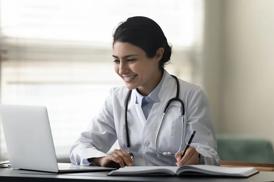 Smiling charge nurse creating a nursing unit schedule in a bright office in front of a window.